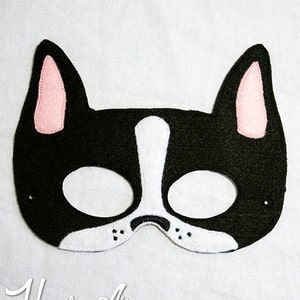 May include: Black felt mask with white and pink details, shaped like a French bulldog. The mask has two eye holes and a white nose.