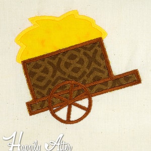 Puede incluir: Un diseño bordado de un carro de heno, con una rueda marrón y una pila de heno amarillo en la parte trasera. El diseño está cosido con hilo marrón y amarillo.