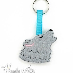 May include: A grey felt wolf head keyring with pink ears, howling, attached to a turquoise ribbon and a silver key ring.