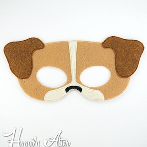 May include: A tan and brown felt dog mask with large brown ears, white accents, and a black nose. The mask is designed to cover the eyes and nose, with eye holes and a nose cutout. The mask is likely for a child's costume or play.
