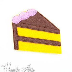 May include: A felt applique of a slice of cake with brown frosting and yellow cake layers. The frosting has pink sprinkles on top.