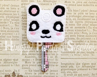 May include: A white panda key chain with black eyes, a black nose, and pink cheeks. The key chain is attached to a silver and black striped key.
