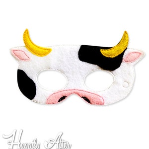May include: A white felt cow mask with black spots, pink accents, and yellow horns. The mask has eye holes and a pink nose. The text "Happily After Designs" is at the bottom.