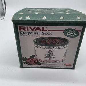 May include: A green and white box for a Rival Potpourri Crock electric simmering cooker. The box features the product name, a picture of the crock, and text that reads "Bonus! Potpourri Mix Included". The box has a Christmas theme.