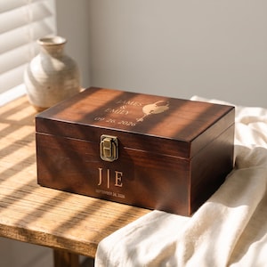 May include: A rectangular dark brown wooden keepsake box with a brass latch. The lid is engraved with "JAMES & EMILY" and "09.26.2026" with a heart-shaped key icon. The front features the initials "J | E" and "SEPTEMBER 26, 2026".