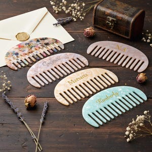 May include: Four semi-circular hair combs made of marbled resin in various colors including multi-color, pale pink, cream, and light blue. Each comb features a personalized name or initials engraved in gold lettering on the curved surface.