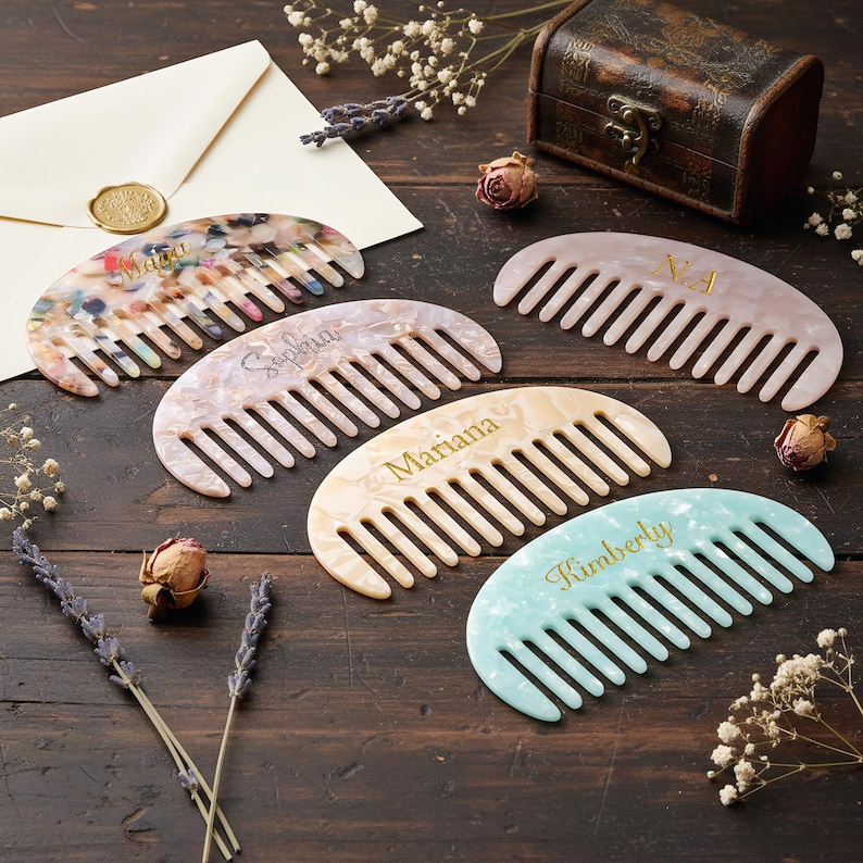 May include: Four semi-circular hair combs made of marbled resin in various colors including multi-color, pale pink, cream, and light blue. Each comb features a personalized name or initials engraved in gold lettering on the curved surface.