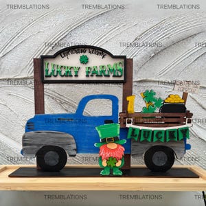 May include: A wooden St. Patrick's Day decoration featuring a blue truck with "Lucky Farms" signage. A leprechaun figure stands in front. The truck bed holds a pot of gold, shamrocks, and a sign that says "Rainbow".