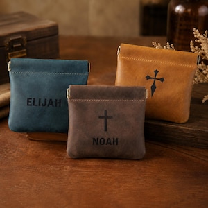 Può includere: Tre piccole pochette in pelle con chiusure in metallo. Una pochette blu è incisa con il nome ELIJAH. Una pochette marrone presenta un simbolo di croce e il nome NOAH. Una pochette color cuoio ha un simbolo di croce decorativo sul davanti.
