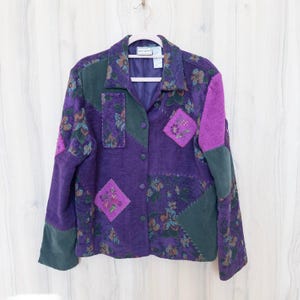 Puede incluir: Una chaqueta de manga larga con botones que presenta un diseño de patchwork en tonos morado, verde oscuro y magenta. La prenda incluye patrones florales, paneles de colores sólidos y detalles de tela en forma de rombo con costuras visibles.