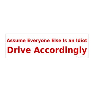 May include: A white rectangular bumper sticker with red text. The text reads "Assume Everyone Else Is an Idiot Drive Accordingly" in a bold, sans-serif font. The website "BumperScholars.com" is in the bottom right corner.