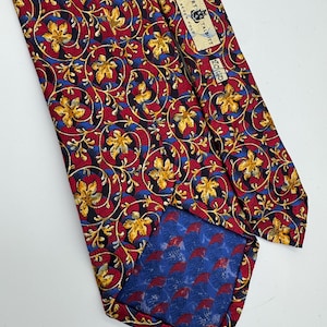 May include: A necktie featuring a repeating pattern of gold leaves and swirling red and blue vines on a black background. The back displays a blue fabric lining with a red leaf pattern, a black label reading SEVEN FOLD, and a Robert Talbott brand tag.