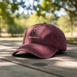 May include: A maroon baseball cap with a curved brim. The cap features a graphic of a pint of beer with a shamrock and the words "Vitamin G" in a gold color.