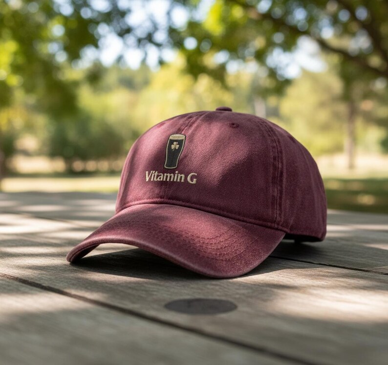 May include: A maroon baseball cap with a curved brim. The cap features a graphic of a pint of beer with a shamrock and the words "Vitamin G" in a gold color.