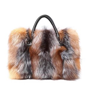 Peut inclure: Un sac à main rectangulaire avec un extérieur en fourrure duveteuse multicolore. La fourrure présente des nuances de marron, d'orange et de gris. Il possède une poignée en cuir noir. Le sac est conçu pour être porté par la poignée.