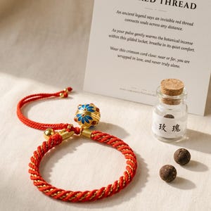 May include: A red and gold twisted cord bracelet featuring a gold-toned spherical locket with blue and red enamel floral patterns. Beside it sits a small glass vial with a cork stopper, containing dark incense pellets and labeled with the Chinese characters for rose.