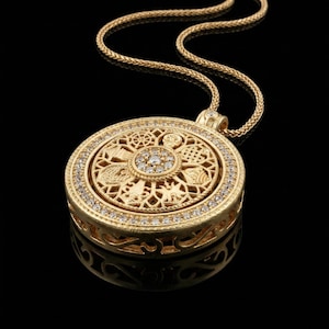 May include: A gold-colored pendant necklace with a detailed, circular design. The pendant features intricate patterns, small diamonds, and a matching gold chain. The necklace is displayed against a black background, highlighting its reflective surface.