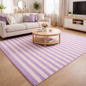 Peut inclure: Un grand tapis rectangulaire à rayures alternées lavande et blanc cassé. Le tapis est posé sur un parquet dans un salon, avec un canapé, une table basse et une télévision en arrière-plan. Le tapis ajoute une touche de couleur à la pièce.