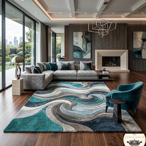 Op de afbeelding: Een moderne woonkamer met een groot vloerkleed met een wervelend patroon in tinten van teal, grijs en beige. De kamer heeft een grijze hoekbank, een teal fauteuil en een open haard. Het vloerkleed meet ongeveer 244 x 305 cm.