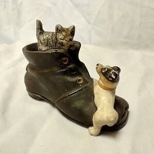 May include: A ceramic figurine of a brown boot with a white dog peeking out from the top and a gray and white cat sitting inside the boot.