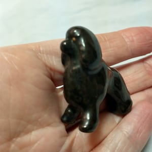 May include: A small black ceramic figurine of a poodle dog. The figurine is standing on all four legs and has a curly tail.