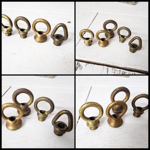 May include: Several antique brass eye bolts with a ring-shaped top and a threaded base are arranged on a white wooden surface. The eye bolts vary slightly in size and finish, showcasing a vintage aesthetic.