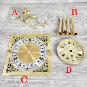 May include: Clock parts, including a gold-toned pendulum, four gold-colored columns, and two clock faces. One clock face is square with the text "HOWARD MILLER", and the other is round with the text "Elgin".