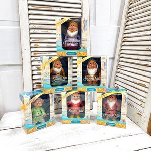 May include: Six vintage Snow White and the Seven Dwarfs dolls in their original boxes. Each doll is a different dwarf: Sneezy, Happy, Sleepy, Dopey, Doc, and Grumpy. The boxes have a blue and gold design with the Snow White logo.