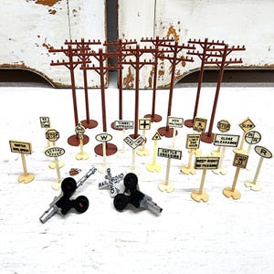 May include: A collection of miniature model train accessories including brown plastic utility poles, various white road signs with black text such as Stop, Speed Limit, and Railroad Crossing, and two black and silver signal light components.