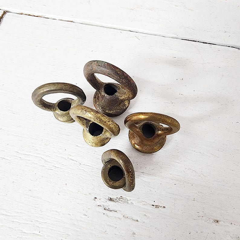 May include: Five antique brass ring pulls with a weathered, aged appearance. Each pull features a circular ring attached to a circular base. The brass has a mix of gold and brown tones, suggesting age and use. These pulls are likely for furniture or cabinetry.
