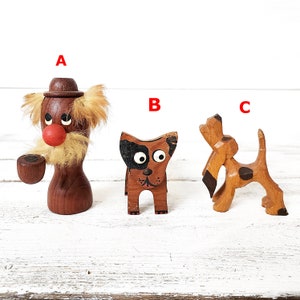 May include: Three wooden figurines, a man with a hat and a mustache, a dog with black spots, and a dog with black eyes. The figurines are painted with brown, black, and white paint.