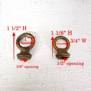 May include: Two antique brass eye bolts. The larger one is 1 1/2 inches high, 1 inch wide, and has a 3/8 inch opening. The smaller one is 1 1/8 inches high, 3/4 inch wide, and has a 1/2 inch opening.