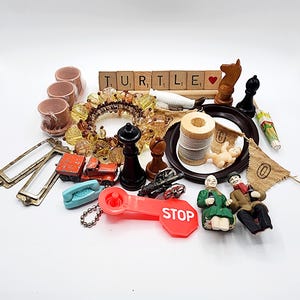 May include: A collection of miniature items including Scrabble tiles spelling TURTLE with a heart, a beaded ring, a red toy truck, a black chess piece, a wooden spool of thread, a red STOP sign keychain, and two small figurines.