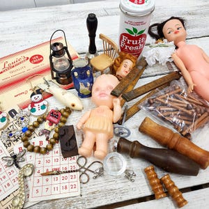 May include: A collection of vintage items including a Fruit Fresh tin, a plastic doll, a miniature wooden chair, a metal lantern, a blue ceramic vase, wooden pegs in a plastic bag, a calendar, a wooden ruler, and various small decorative trinkets.