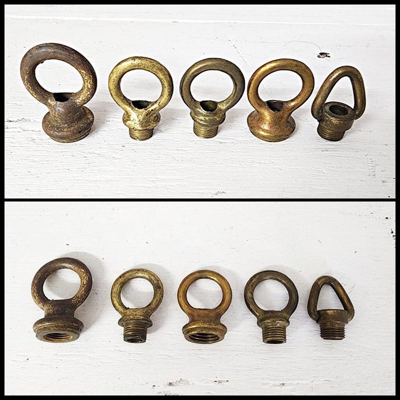 May include: A collection of antique brass eye bolts with threaded bases. The eye bolts vary in size and shape, with a mix of round and triangular eyelets. The metal has a tarnished, aged appearance, suggesting vintage or reclaimed hardware.
