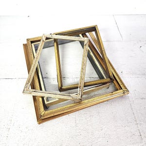 May include: A collection of antique picture frames in various sizes and finishes. The frames are primarily gold and cream-colored, with ornate detailing. Some frames have glass inserts, while others are empty.