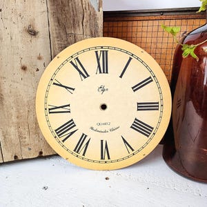 May include: A vintage clock face with a cream-colored background and black Roman numerals. The clock face has the word "Elgin" in script and the words "Quartz Westminster Chime". The clock face is round.