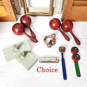 May include: A collection of musical instruments, including red wooden maracas, a small harmonica with "Chicago Blues" text, a wooden tambourine, and a pair of green and blue percussion instruments. The word "Choice" is written in red.