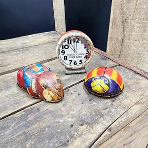 May include: Three vintage tin toys: a red, blue, and yellow bug, a ladybug with a yellow face, and a clock with the text "Kiddie Clock Dime Bank".