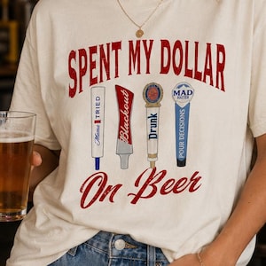 以下が含まれることがあります： 「Spent My Dollar On Beer」の赤い文字が入ったクリーム色のTシャツ。 「Blackout」や「Pour Decisions」などのフレーズが書かれた4つのビールタップのイラストが特徴です。 背景には「Cold Beer」と書かれたネオンサインがあります。