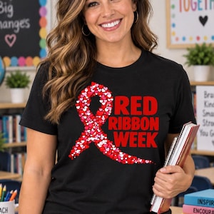 Op de afbeelding: Een zwart T-shirt met korte mouwen en een grote rode lintafbeelding bestaande uit vele kleine rode, roze en witte hartjes. Rechts van het lint staat de tekst RED RIBBON WEEK in dikke rode hoofdletters. Het T-shirt heeft een ronde hals.