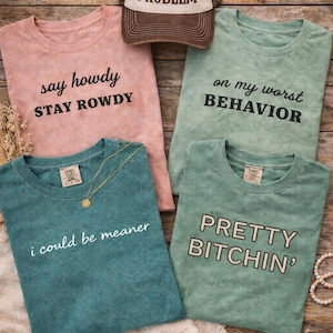 Può includere: Un pacchetto di cinque magliette e un cappellino da camionista con frasi umoristiche. Le magliette sono in rosa, verde acqua e verde, ognuna con una frase diversa in grassetto. Il cappellino da camionista è marrone e bianco con la scritta "Somebody's PROBLEM".