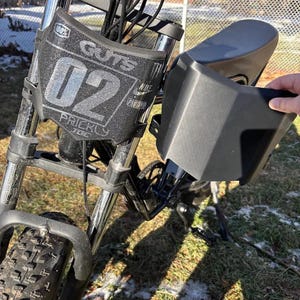 Könnte beinhalten: Ein schwarzes und silbernes Elektrofahrrad mit einem vorderen Nummernschild mit der Aufschrift "Guts 02 Prickly Joe". Das Fahrrad hat einen schwarzen Sitz und Lenker sowie einen dicken Vorderreifen. Das Bild ist im Freien aufgenommen.