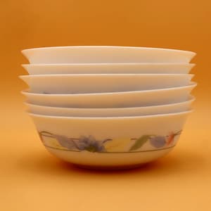 May include: A stack of five white ceramic bowls with a smooth, rounded shape. The bottom bowl features a decorative band around the exterior, displaying a pattern of blue and purple flowers with green leaves and thin horizontal lines.