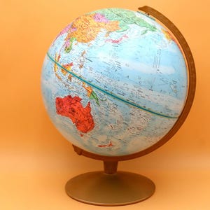 May include: A vintage globe with a blue ocean and colorful continents. The globe is mounted on a gold-colored metal base and has a wooden frame. The globe is a classic educational tool.