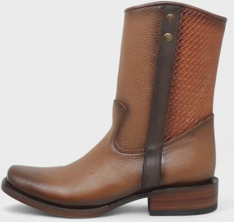 Pu&ograve; includere: Stivale in pelle marrone con punta quadrata e tacco basso. Lo stivale presenta un pannello strutturato sul lato e una cinghia in pelle marrone scuro con due bottoni decorativi. Lo stivale &egrave; alto circa 20 cm.