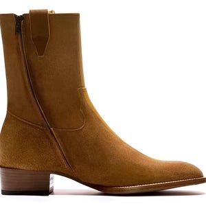 May include: A tan suede ankle boot with a side zipper. The boot has a stacked heel and a pointed toe. The boot is a neutral color and would be suitable for many outfits. The boot is a classic style.
