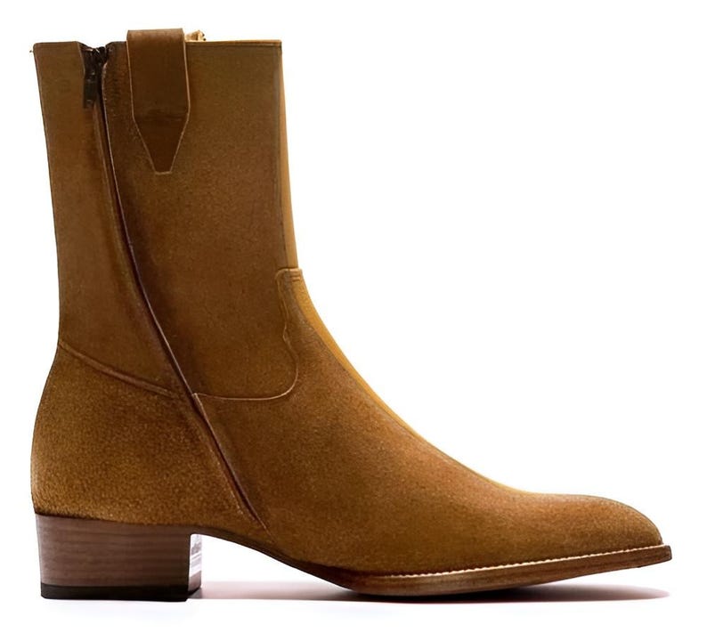 May include: A tan suede ankle boot with a side zipper. The boot has a stacked heel and a pointed toe. The boot is a neutral color and would be suitable for many outfits. The boot is a classic style.