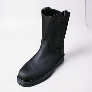 Peut inclure: Botte de travail en cuir noir avec un bout arrondi et une tige mi-mollet. La botte a une semelle robuste et une boucle de tirage en haut. La botte est conçue pour la durabilité et la protection.