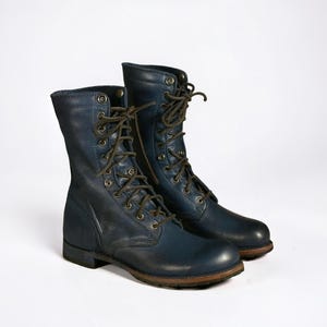 May include: A pair of navy blue leather combat boots with brown laces and soles. The boots are mid-calf length and have multiple eyelets for the laces. The leather has a slightly distressed appearance.